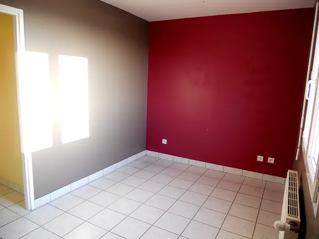 Pièce claire d’un T3 en duplex, carrelage blanc et mur rouge